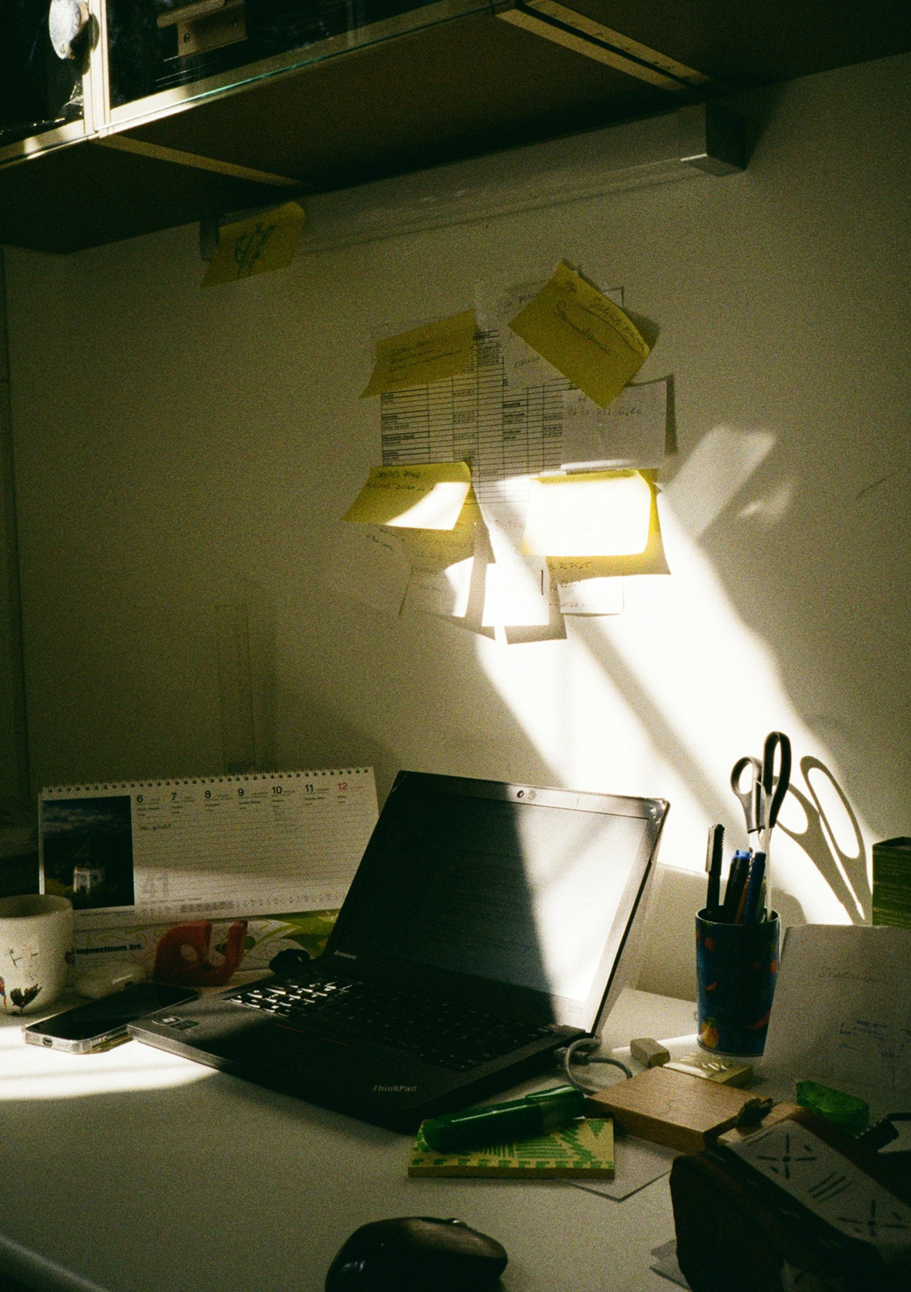 Cluttered workspace with laptop, calendar, and sticky-note reminders illustrating adult ADHD organization challenges